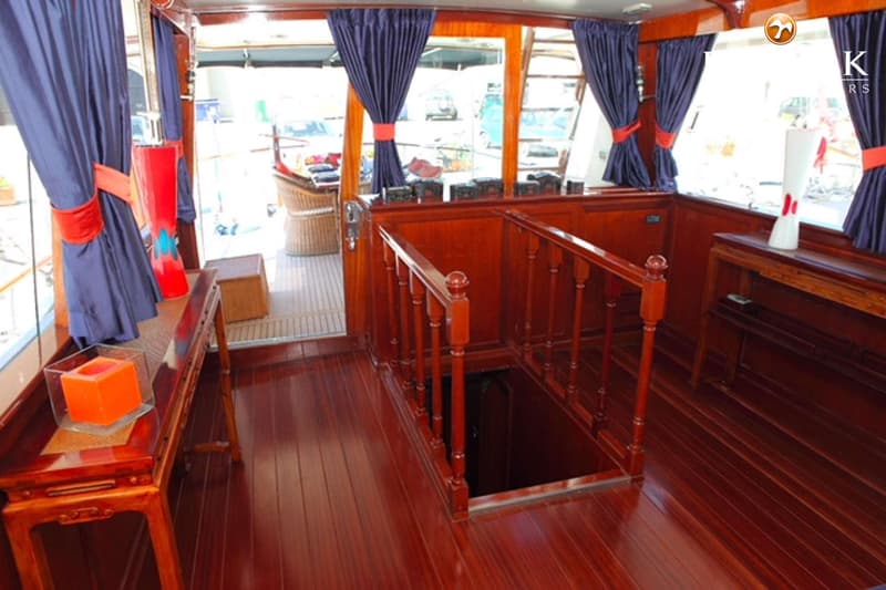 De foto toont een interieur van een boot met glanzende houten vloeren en wanden, blauwe gordijnen en een trap naar beneden.