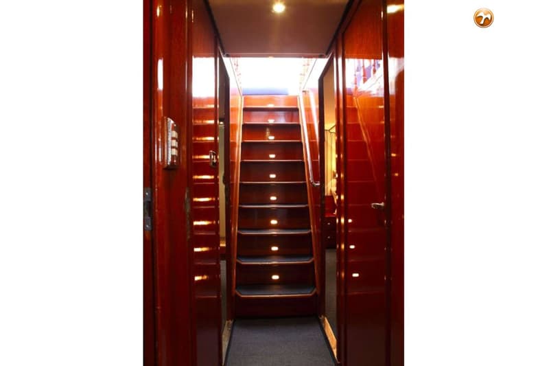 Een houten trap met verlichting in de treden leidt omhoog, geflankeerd door houten wanden en deuren.