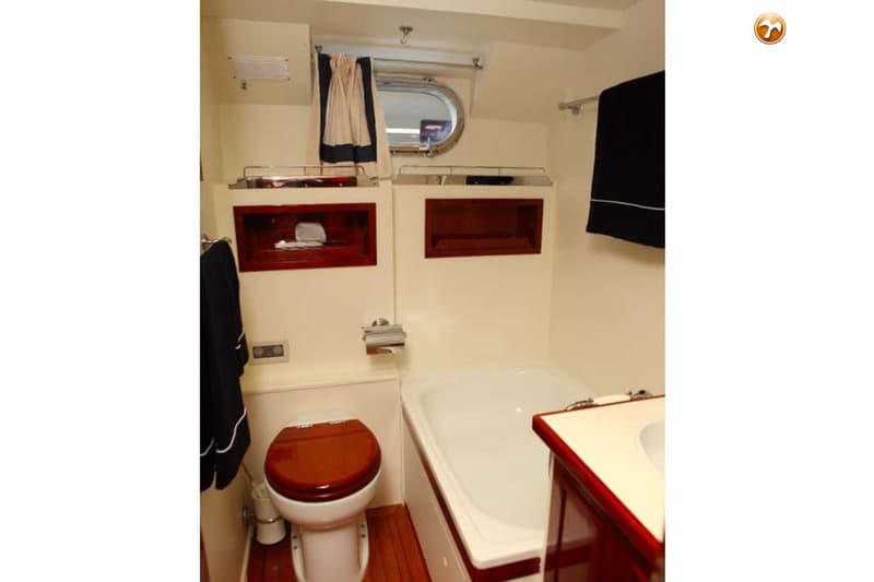 Een badkamer in een boot met een toilet, bad, wastafel en een patrijspoort met gordijn. — Baglietto Maiorca