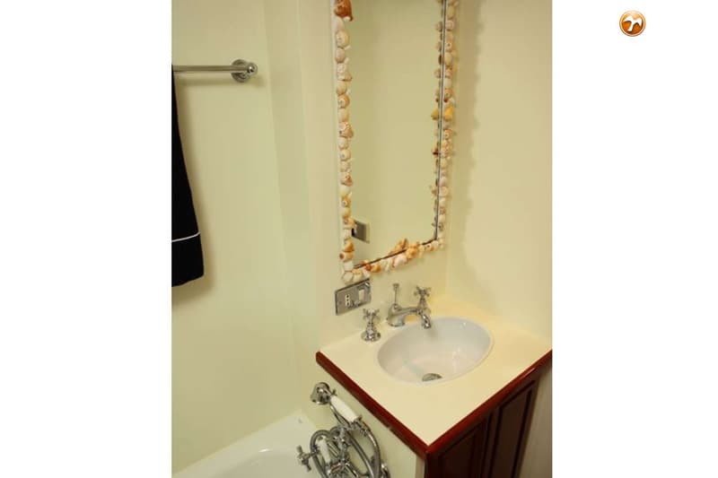 Een badkamer met een spiegel omrand met schelpen, een wastafel met kraan, en een deel van een badkuip met douchekop.