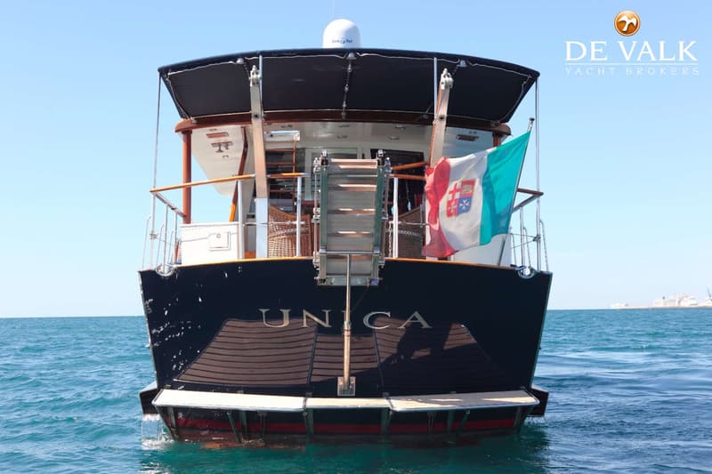 De achterkant van een donkerblauwe boot met de naam "UNICA" erop, een Italiaanse vlag en een zwemtrap. — Baglietto Maiorca