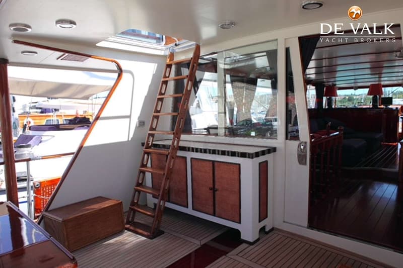 Een houten ladder leidt naar een open luik, met een kastje en een houten kist ernaast, en een doorgang naar een interieur.