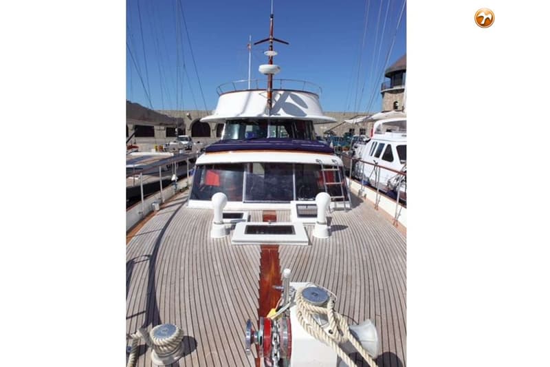 Een dek van een boot met houten planken, een ankerlier, touwen, en de kajuit met ramen en een ladder. — Baglietto Maiorca