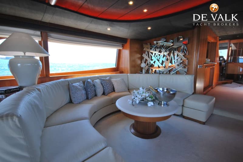 Een interieur van een boot met een crèmekleurige ronde bank, een ronde tafel met bloemen en een ijsemmer, en een raam met…