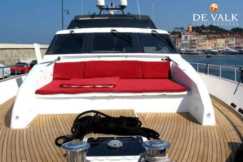 Een witte boot met een teakhouten dek en rode kussens op de boeg, met een dorpje op de achtergrond. — Couach 2800 Fly