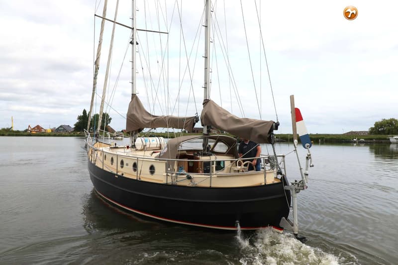 Een zeilboot met twee masten en opgerolde zeilen vaart op een waterweg, met een persoon aan het roer. — Danish Rose 42