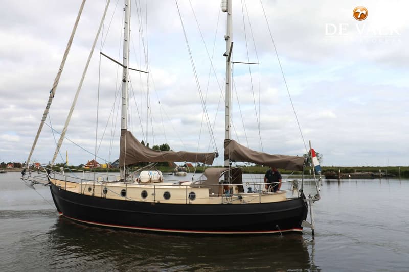 Een donkerblauwe zeilboot met beige opbouw en twee masten vaart op een waterweg. — Danish Rose 42