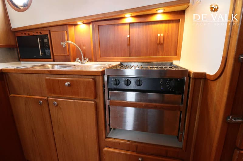 Een houten scheepskeuken met een gootsteen, kraan, magnetron, gasfornuis met oven en diverse kastjes.