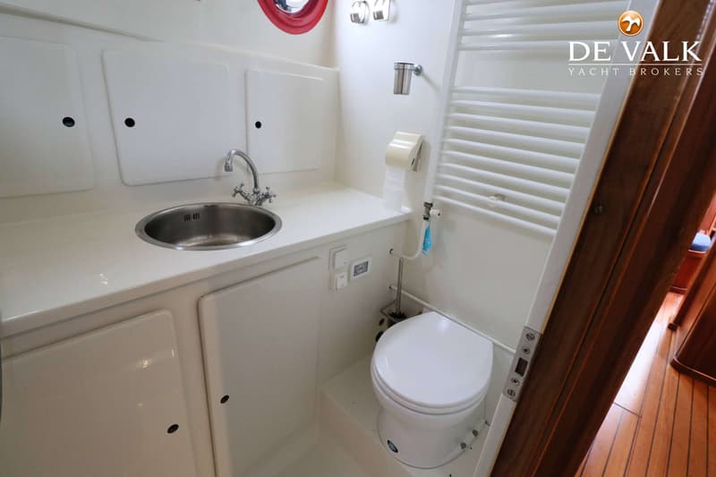Een witte badkamer met een wastafel, toilet, handdoekrek en een rood patrijspoort.