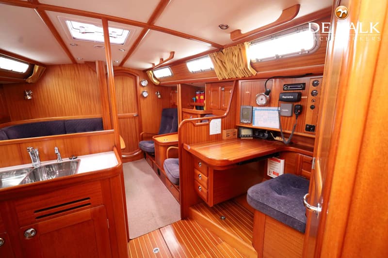 De foto toont het interieur van een boot met houten afwerking, een kombuis, een navigatiehoek en zitplaatsen. — Malo 37
