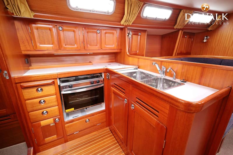 Een houten kombuis met een dubbele spoelbak, een fornuis met oven, en diverse kasten en lades.