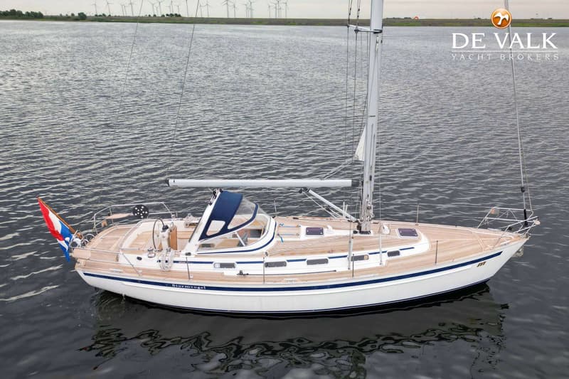 Een witte zeilboot met een blauwe streep en houten dek ligt in het water, met windmolens op de achtergrond. — Malo 37