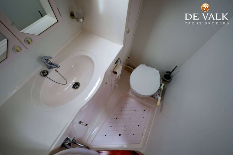 Een witte badkamer met een wastafel, spiegel, toilet en een douchebak met een rooster.