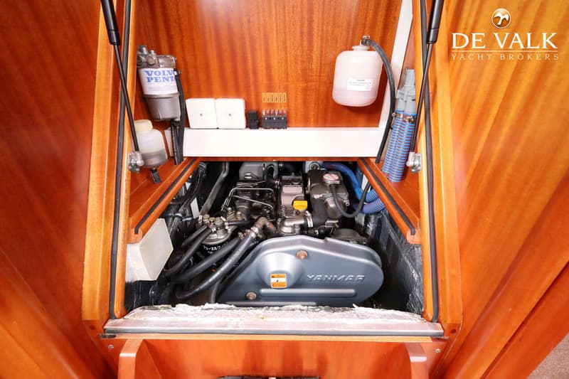 De foto toont een Yanmar scheepsmotor in een houten motorruimte, met een Volvo Penta filter en diverse slangen en bedrading.