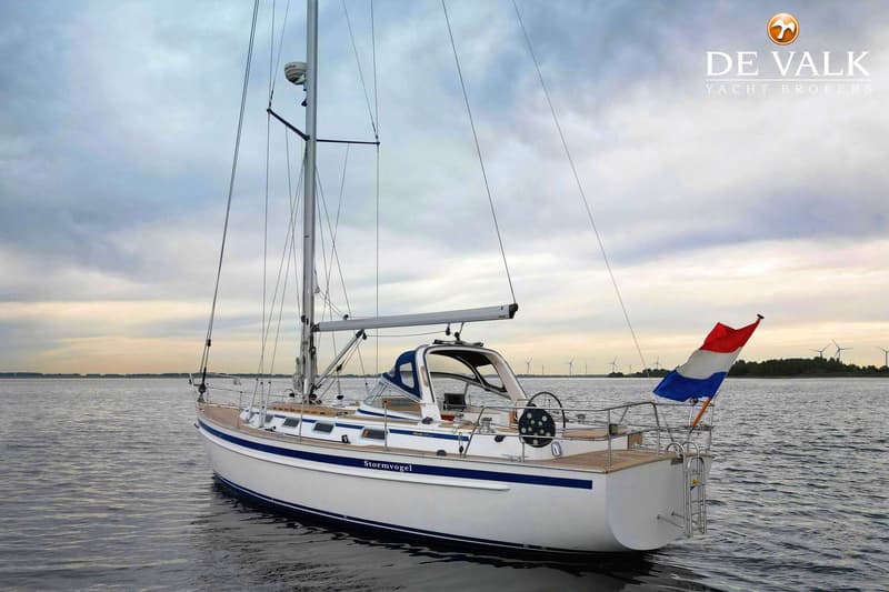 Een witte zeilboot met blauwe strepen en de naam "Stormvogel" ligt op het water onder een bewolkte lucht. — Malo 37