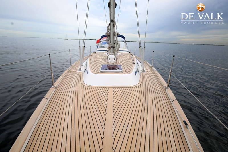 Een zeilboot met een houten dek en een mast in het midden, varend op rustig water onder een bewolkte lucht. — Malo 37