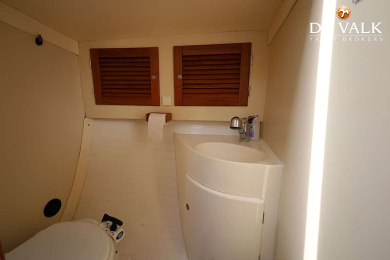 De foto toont een kleine badkamer met een toilet, een hoekwastafel met kraan en twee houten luiken.