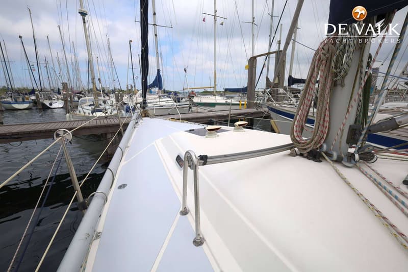 Een bovenaanzicht van het dek van een zeilboot met een mast, touwen en andere boten in een haven. — Hanse 401