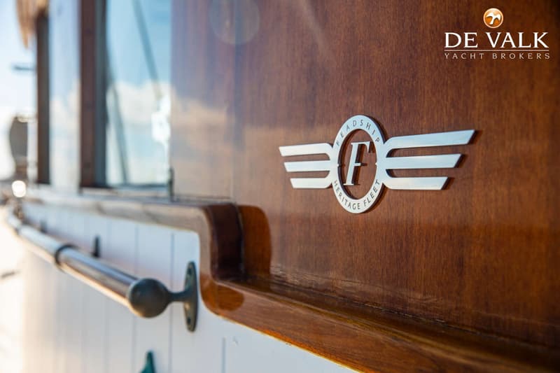 Een detail van een houten boot met een zilverkleurig "Feadship Heritage Fleet" logo en een handgreep. — Feadship Ketch