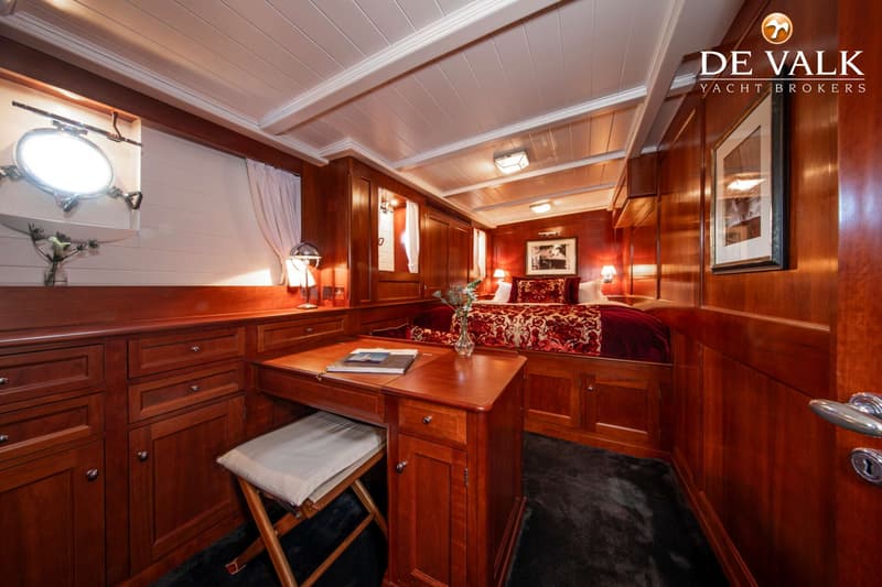 Een slaapkamer met een tweepersoonsbed, een bureau met kruk, een patrijspoort en houten lambrisering.