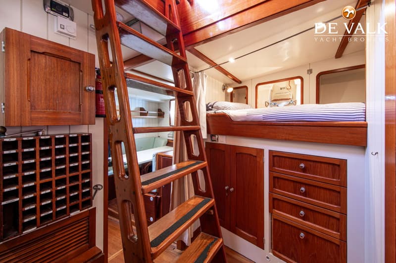 Een houten trap leidt naar een slaapgedeelte met een bed en er zijn diverse houten kasten en lades zichtbaar.