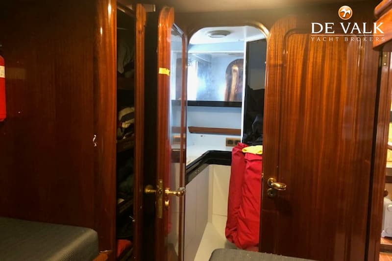 Een interieurfoto van een boot met houten wanden en deuren, een open kast met kleding en een brandblusser. — CCYD 75