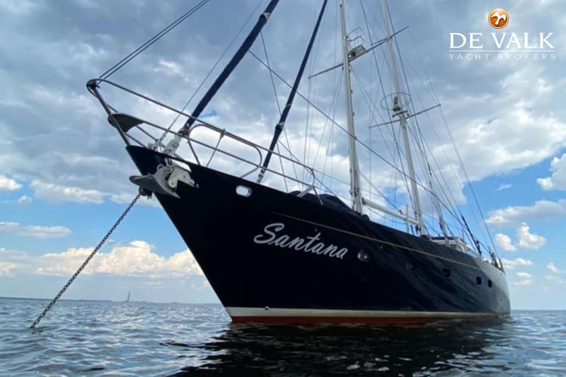 Een donkerblauwe zeilboot met de naam "Santana" op de boeg ligt voor anker in het water onder een bewolkte lucht. — CCYD 75
