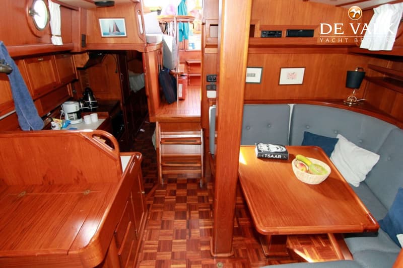 Een interieur van een boot met houten lambrisering, een zithoek met tafel, een kombuis en een trap naar een hoger dek.