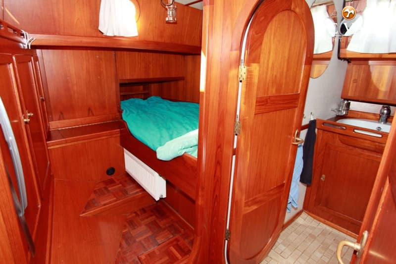 Een houten interieur van een boot met een bed met turquoise dekbed en een badkamer met wastafel. — Volkerak 46