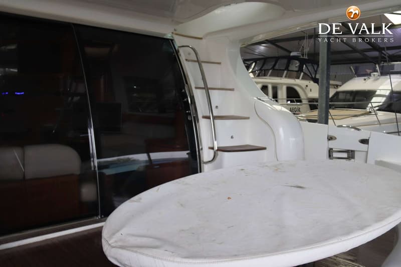 Een witte boot met een trap, een donker raam en een afgedekte tafel, met andere boten op de achtergrond. — Azimut 68 Plus