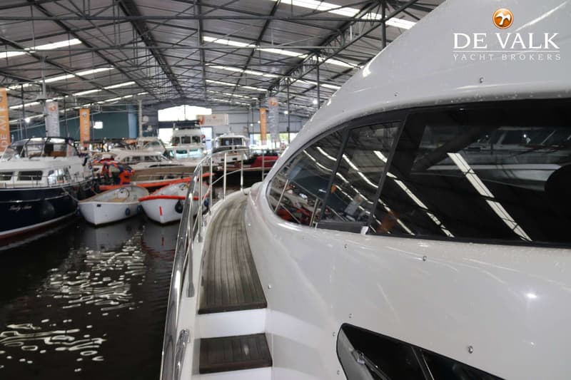 Een witte boot met houten dek en reling, liggend in een overdekte hal met andere boten. — Azimut 68 Plus