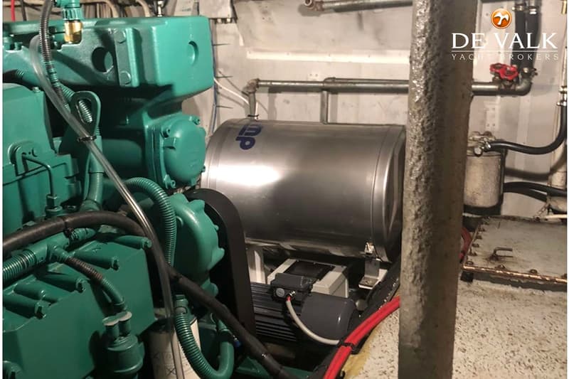 Een groene motor met een zilveren boiler en diverse leidingen en kabels in een machinekamer.