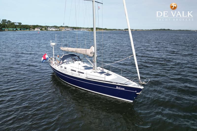 Een blauw-witte zeilboot met de naam "Balans" vaart op open water, met een persoon aan boord en een Nederlandse vlag.