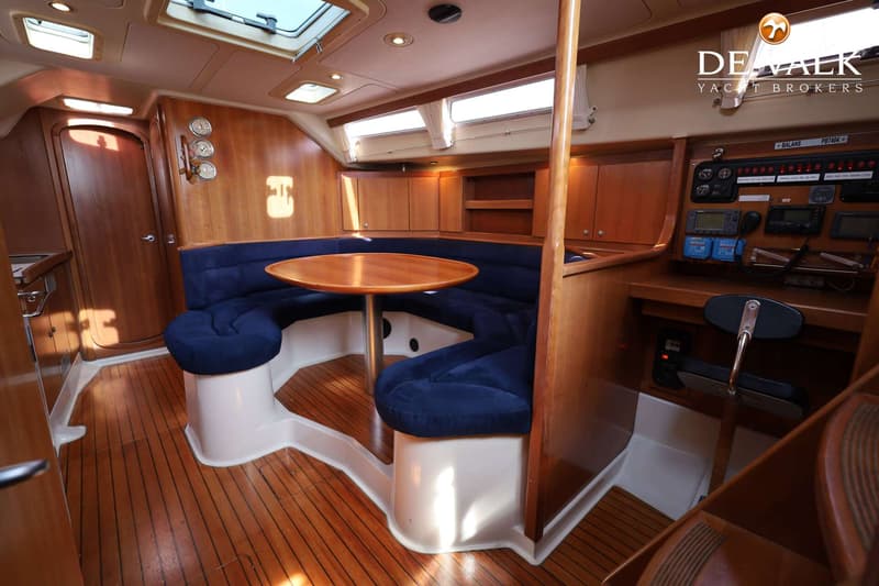 Een interieur van een boot met een houten vloer, een ronde houten tafel en een U-vormige blauwe bank. — Dehler 41 Cruising