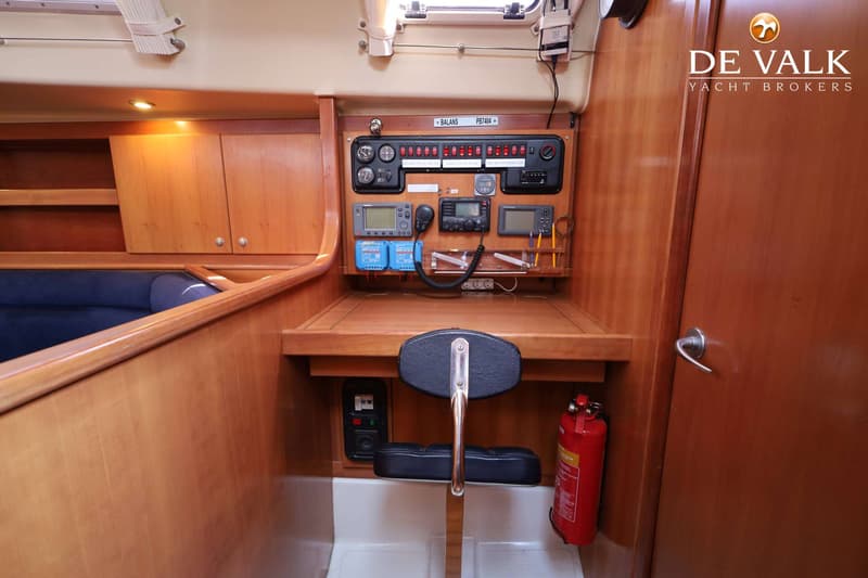 Een houten interieur van een boot met een navigatiehoek, stoel, brandblusser, en een bank met blauwe kussens.
