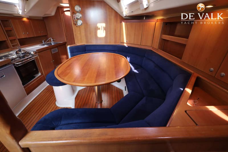Een houten interieur van een boot met een kombuis, een U-vormige blauwe bank en een ovale houten tafel. — Dehler 41 Cruising