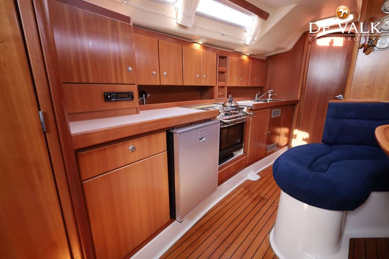 Een houten kombuis met een fornuis, oven, koelkast, gootsteen en opbergkasten, met een blauwe zitting op de voorgrond.