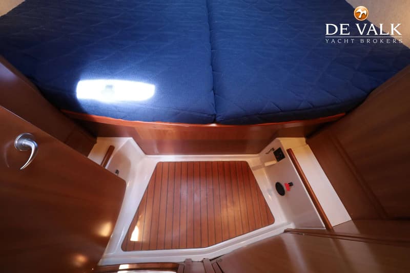 De foto toont een kajuit met een donkerblauw matras, een houten vloer en zijwanden, en een zilverkleurige handgreep.