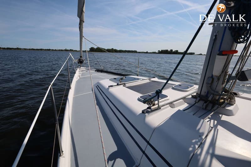 Een wit zeiljacht vaart op een meer met een blauwe lucht en een groene oever op de achtergrond.