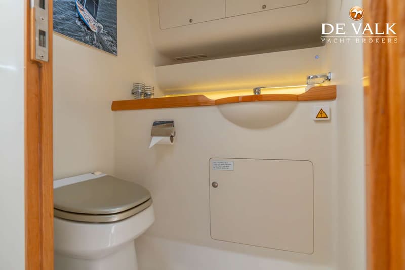 Een toiletruimte met een toilet, wastafel, spiegel, toiletrolhouder en een foto van een zeilboot aan de muur.