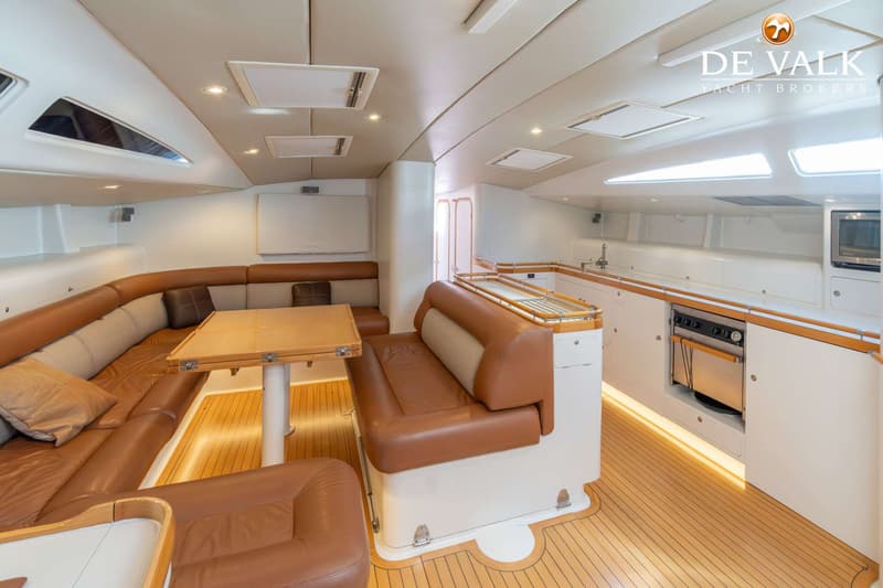 De foto toont het interieur van een boot met een zithoek, een tafel en een kombuis met een fornuis en spoelbak.