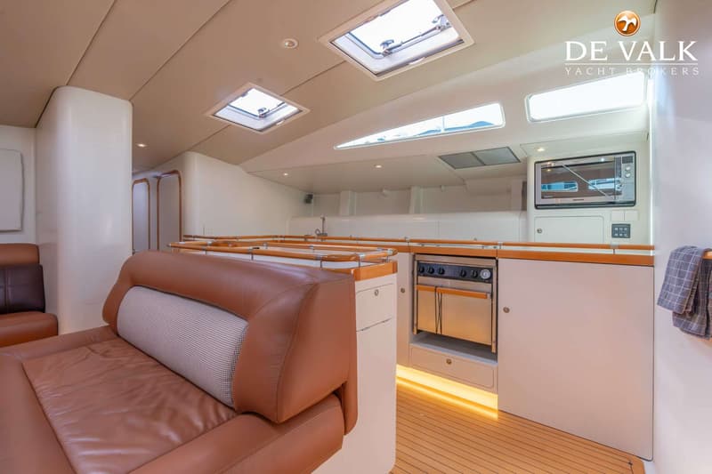 De foto toont een interieur van een boot met een bruine lederen bank, een kombuis met een oven, magnetron en gootsteen.
