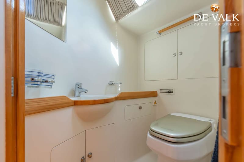 Een witte badkamer met een wastafel, toilet en opbergkasten, met houten accenten en een spiegel.