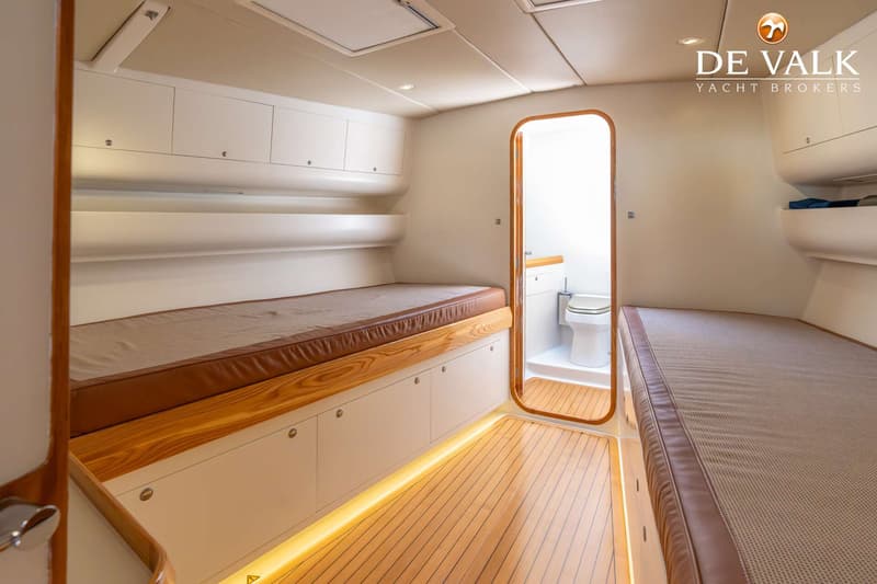 De foto toont een kajuit met twee bedden, een houten vloer en een open deur naar een toiletruimte. — Marten Judel Vrolijk 60
