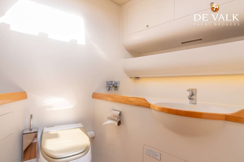 Een witte badkamer met een toilet, wastafel, spiegel, opbergkastjes en een houten afwerking.