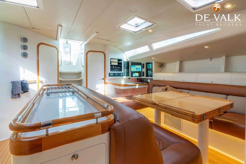 De foto toont het interieur van een jacht met een kombuis, navigatiehoek en zithoek met een houten tafel.