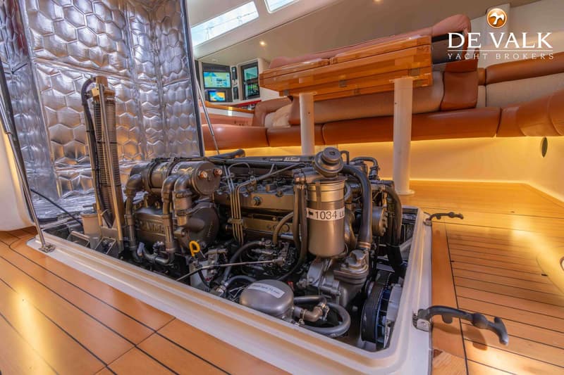 Een gedetailleerde foto van een scheepsmotor in een motorruimte met een houten vloer en een bank in de achtergrond.