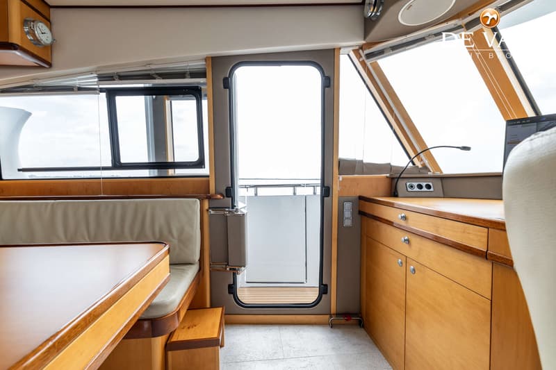 Een interieur van een boot met een houten tafel, banken, een deur, ramen en een stuurstand met een monitor. — Jetten Custom