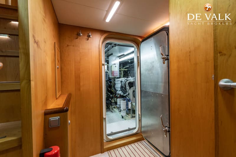 Een houten interieur met een open metalen deur die toegang geeft tot een machinekamer.