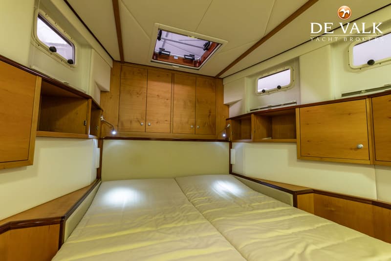 De foto toont een slaapkamer in een boot met een tweepersoonsbed, houten kasten en patrijspoorten. — Jetten Custom
